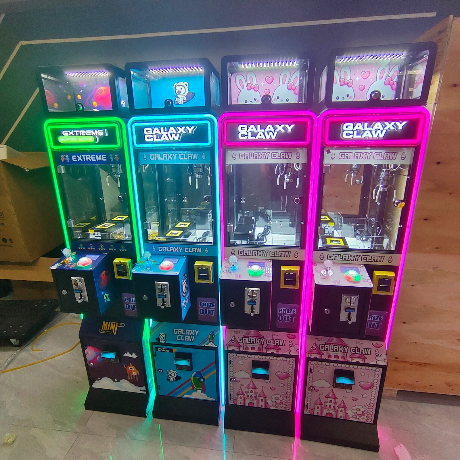 Four colorful mini claw machines with illuminated green, blue, and pink borders